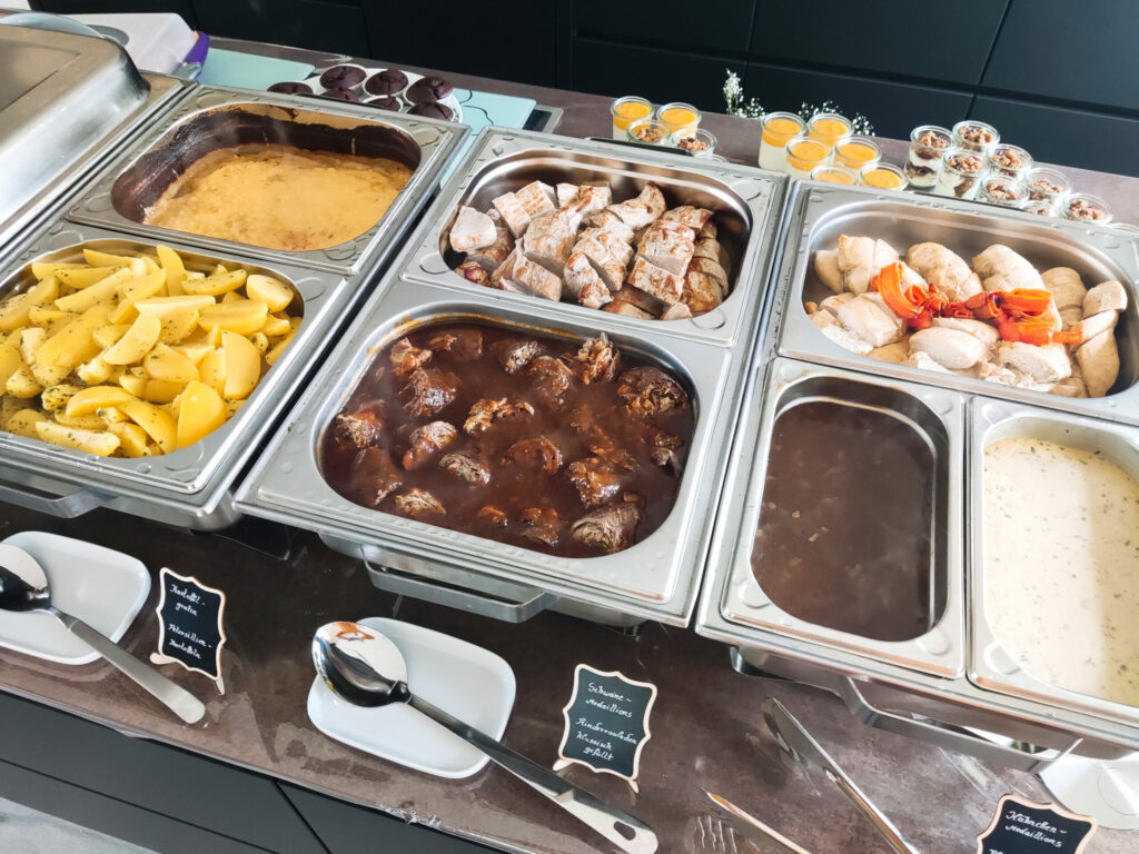 Ein vielseitiges Buffet von Klein Catering mit warmen Hauptgerichten wie Fleischbällchen, Gemüsebeilagen, Kartoffeln und verschiedenen Saucen, perfekt für Events